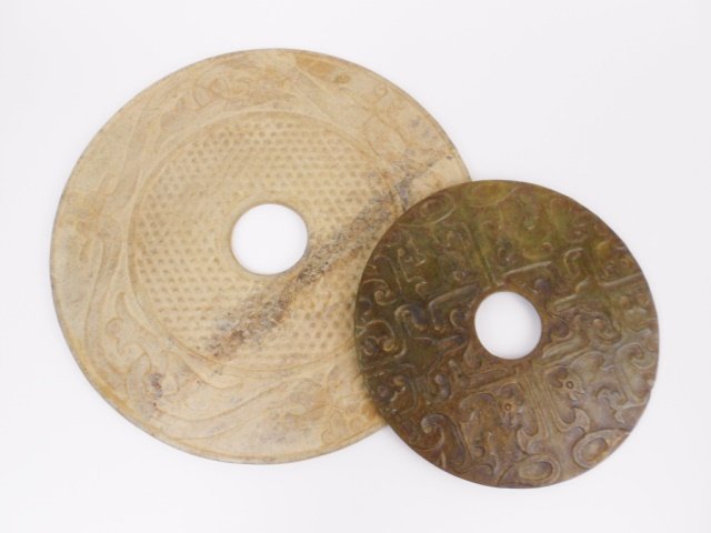 Antique Chinese Jade Bi Discs: Two circular Chinese jade bi discs. Largest measures 11" in diameter and carries anthropomorphic mask and stylized ox designs. Smaller bi is of mottled green color, having dragon and phoenix designs c