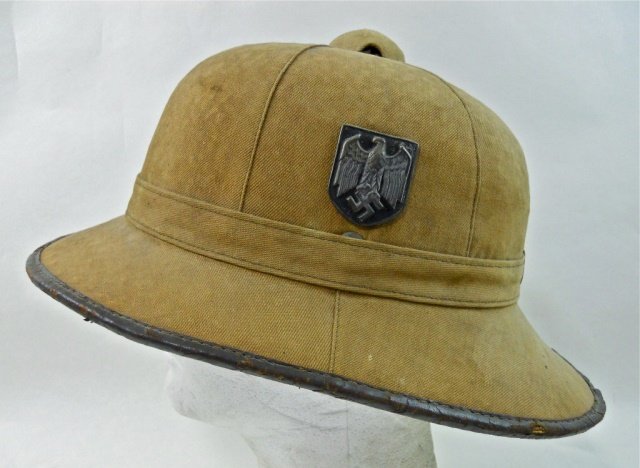 WWII German DAK Type I Canvas Pith Helmet: Canvas over cork construction with Wehrmacht insignia and national shield. Leather border with leather interior band, red cloth interior with metal vent at crown. Well worn with soiling. Scattered lea