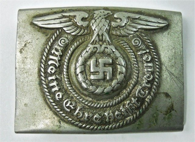 WWII German SS Belt Buckle, O & C: Die struck nickel construction with spread winged eagle clutching wreathed swastika, two rope borders surround gothic script, "MEINE Enre heist Treve!" Reverse with two prong catch and soldered catch.