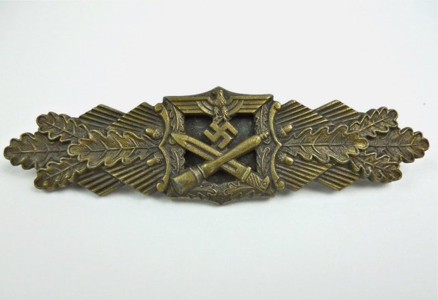 WWII German Wehrmacht Close Combat Clasp, Peekhaus: Two piece die struck badge, signed on reverse, "FEC W.E. PEEKHAUS BERLIN AUSF A.G. M.U.K. GABLONZ", with tapered fat pin. Bronze finish with crossed bayonet and stick grenade surmounted by spread wing