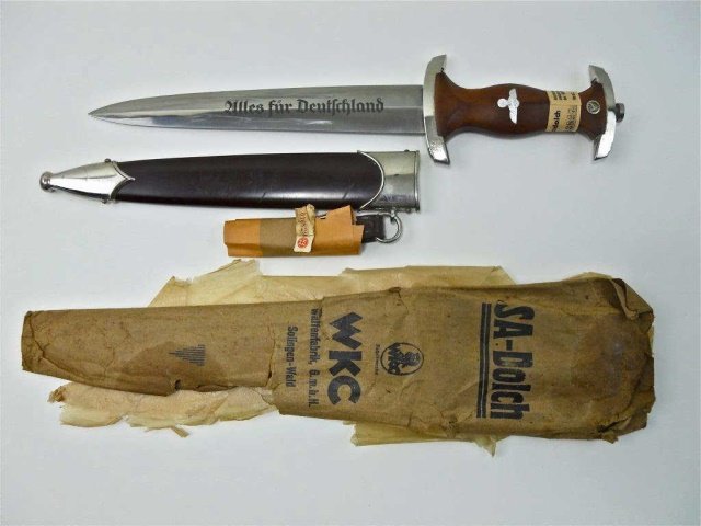 WWII SA Dress Dagger, with Tag and Bag RZM 7/42: Mint, unissued SA dagger by WKC. RZM type with plated guards with wood grip , NSDAP eagle and enamel button with SA blade etched, "Alles fur Deutschland" in gothic script. Reverse is marked, "RZM 7/42