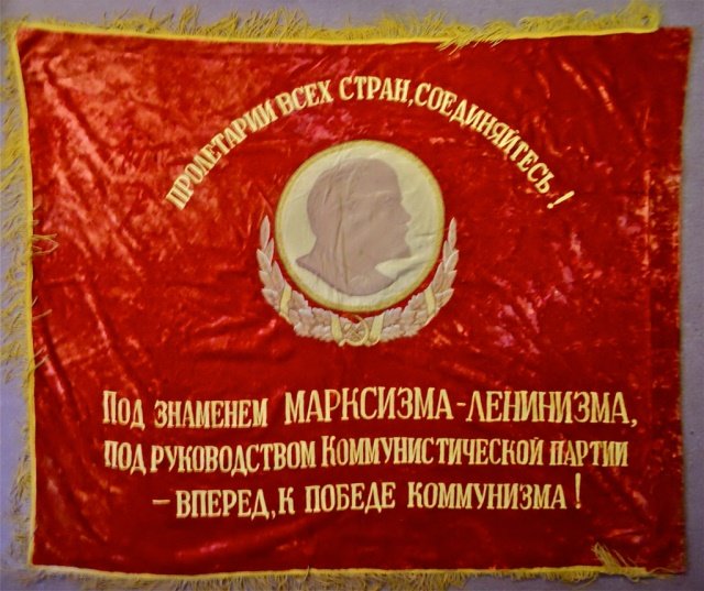 Soviet Military Parade Banner: Double-sided red velvet banner with yellow stitching and 4" yellow fringe. Obverse depicts center portrait of Lenin in silk, with embroidered communist slogan. Reverse features a hammer and sickle wit