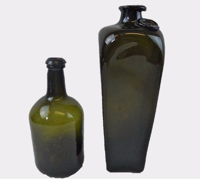 Two 18th C. Black Glass Spirit Bottles: One hand blown dark olive glass mallet form spirit bottle, sand pontil base with double lip and scattered bubbles in glass. 8.4"H x 4"D. One hand blown dark olive glass sealed case gin. Pig snout form