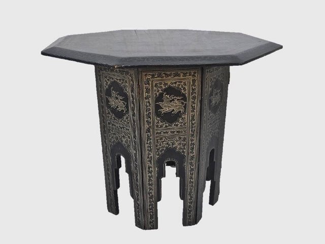 Asian Carved Wood Table: Southeast Asian carved collapsible occasional table. Ebonized with incised carved decoration of mythological beasts and traditional scenes. Some wear to edges, top with crack. Measures 26"H x 30"W.