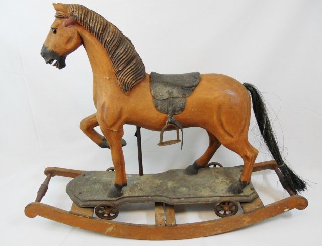 Antique Wooden Rocking Horse: Antique carved wooden rocking horse. Originally mounted on board with cast iron wheels. Leather saddle with cast iron stirrups and horse hair tail. Measures 25" H x 33" W