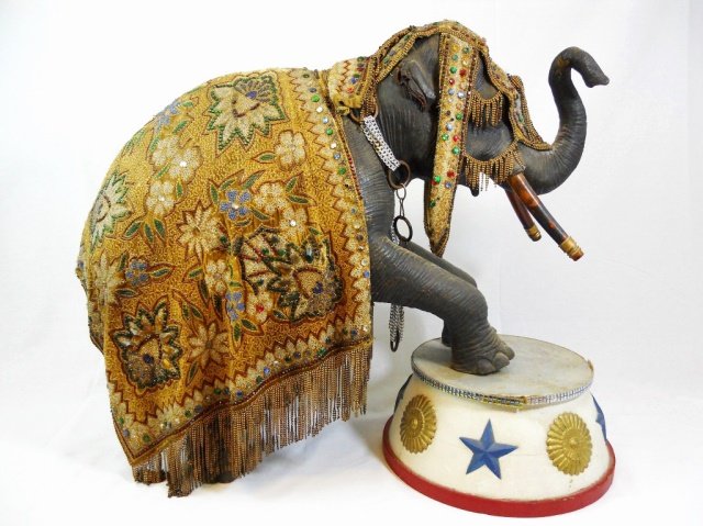 Antique Wooden Costumed Circus Elephant: Antique wood figure in the form of a rearing elephant with painted surfaces. The figure is adorned in an ornately beaded velvet and silk circus costume, with 6" H painted and embellished stand underfo