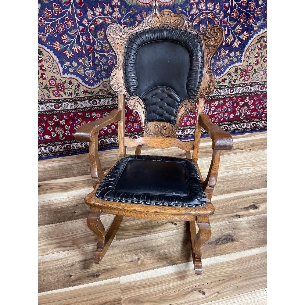 HEAVILY CARVED SOLID OAK ROCKING CHAIR: LEATHER BACK AND SEAT WITH BRASS TACKS. SMALL PIECE OF VENEER MISSING A SMALL PIECE OF VENEER AT TOP.