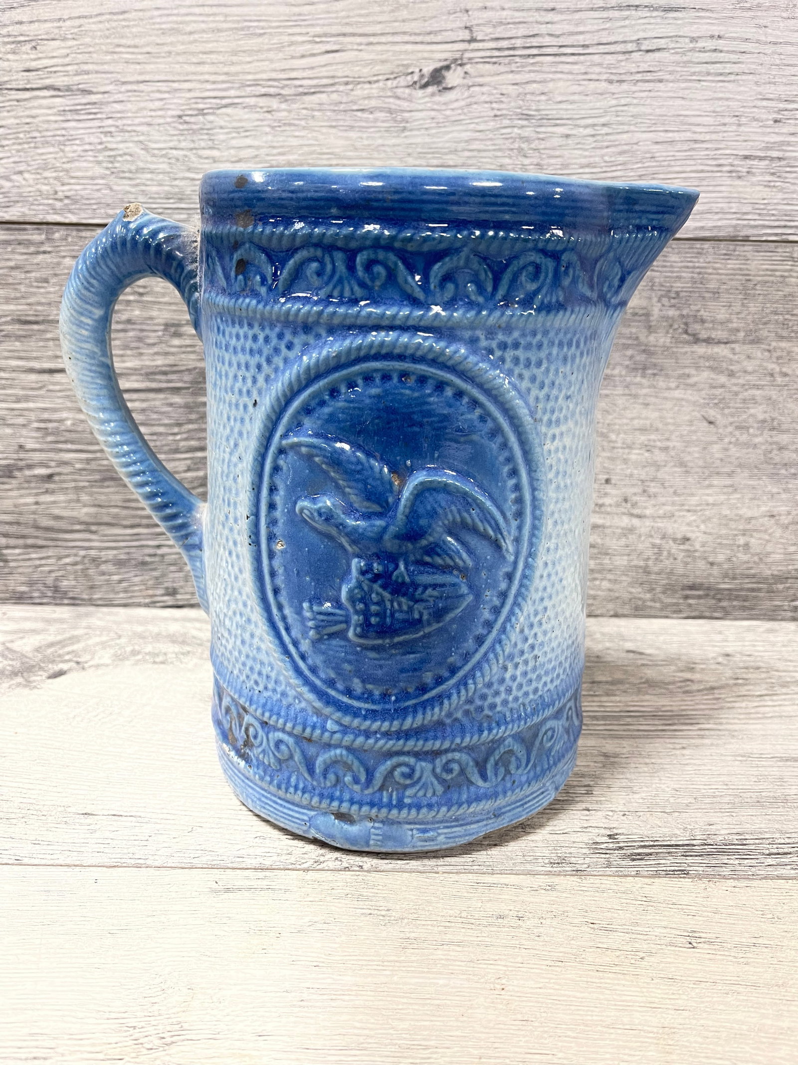 ANTIQUE SALT GLAZED STONEWARE PITCHER: EAGLE ON SHIELD. MIRROR CHIPS AND HAIR LINE CRACK. 8"T