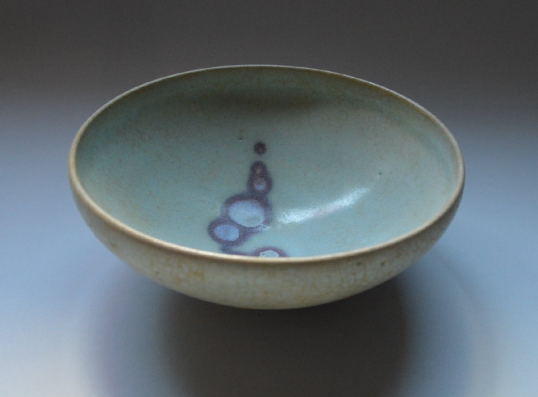 A Song Ming Dynasty Jun Yao Bowl: Thick sky blue milky glaze running down the sides stopping above the foot. Palm eyes, worm tracks, and iron oxide crazing. Nicely flared foot burnt brown in the wood firing. A copper glaze splash of m