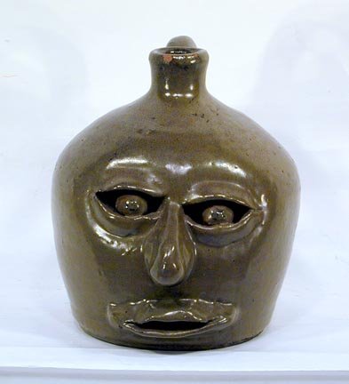 Lanier Meaders Early Face Jug: circa 1960's. Matte green glaze. Chigger bite size chip on glaze on rim. 8" h. It is difficult to distinguish between Lanier and Cheever's face jugs. Signature in glaze at bottom.