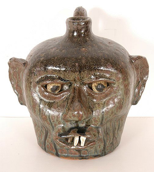 Lanier Meaders, Face Jug w China Plate Teeth.: RARE. c. 1960's. Early, primitive clay eyes. Early tobacco-spit glaze with frog green drips is one of the best we have ever seen. Primitive flat ears. 8"h. Mint condition. Est. $4,000 - $6,000. Ship:
