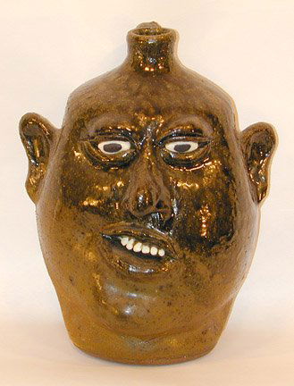 Lanier Meaders, Face Jug w Crooked Smile.: c. late 1980's. High tobacco-spit glaze. 11" h. Provenance: Chuck and Jan Rosenak. Mint condition. Est. $1,200-2,000. Ship: $50