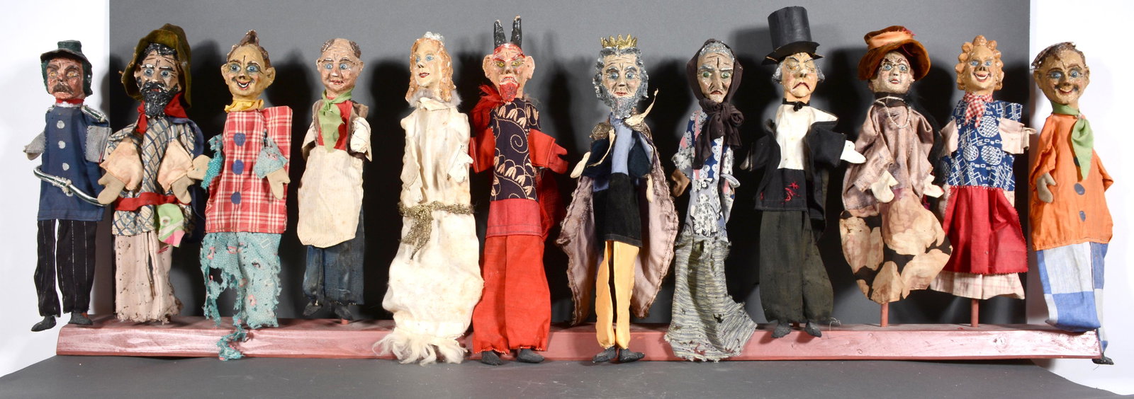 12 Early Puppets.: 12 Early Puppets. Not signed. Carved wood and paper mache puppets with handmade costumes. Some loss and minor damage, otherwise good to fair condition. Average size is 17" h. Display stand is 57" long