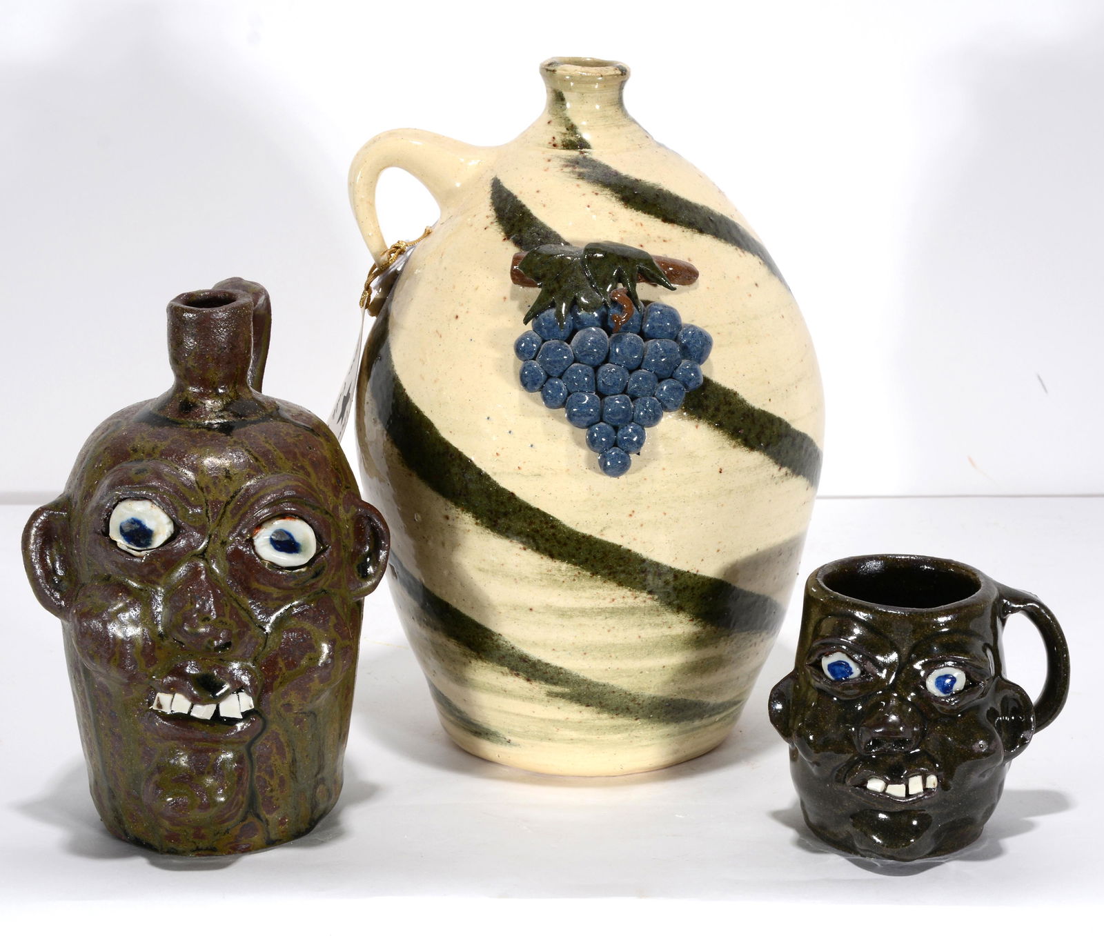 Hewell Family. Face Jug, Grape Jug & Face Cup.: Grace, Harold and Todd Hewell. Face Jug, Grape Jug and Face Cup. 1999. Signed and dated. Mint condition. Tallest is 10”h. Est. $200-300. Ship: $75