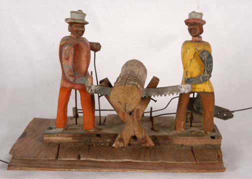 Two Men Sawing.: Part of an early whirligig. Two different motions. One makes men saw, the other makes the mens' heads turn. Carved and painted wood with tin. Face has plastic features. Missing fan, otherwise working 