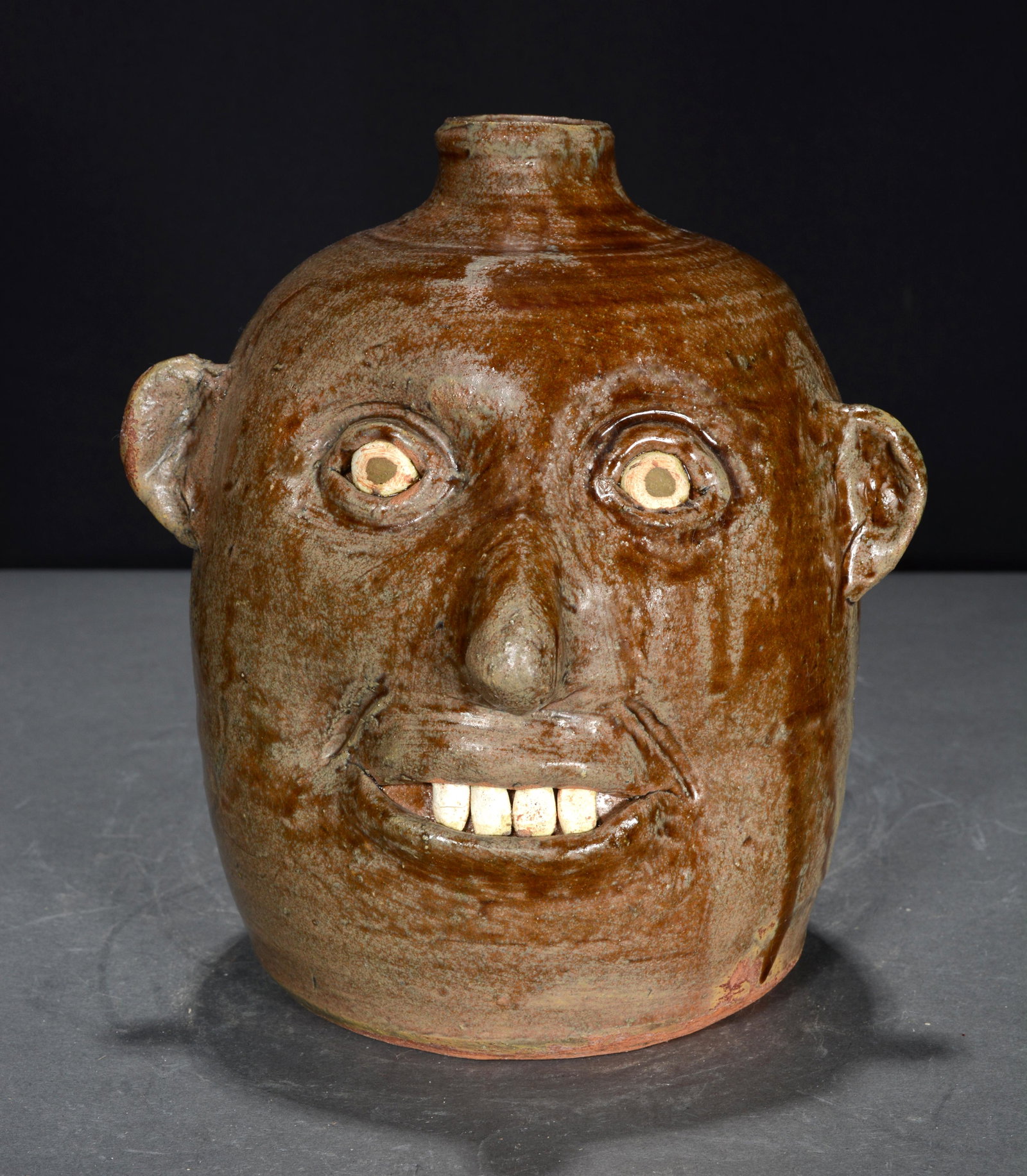 Reggie Meaders. Celebration Face Jug With 4 Teeth.: Reggie Meaders. 100-Year Celebration Face Jug With Four Teeth. Signed in script with dates 1890-1990. 7.5"h. Est. $200-300. Ship: $45
