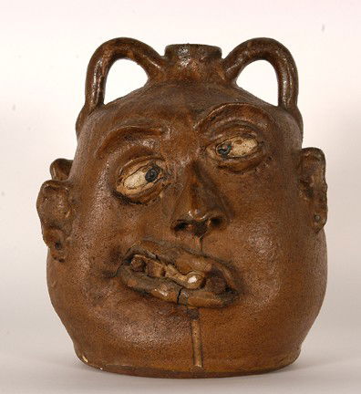 Lanier Meaders. Dbl. Face Rock Tooth Jug.: Crossed Eyed. Hand-dug clay with granite and quartz teeth. c. 1968-69. Experimental glaze. Thick and heavy-handed glaze with a single drip. One side is cock-eyed and the other side is looking left wit