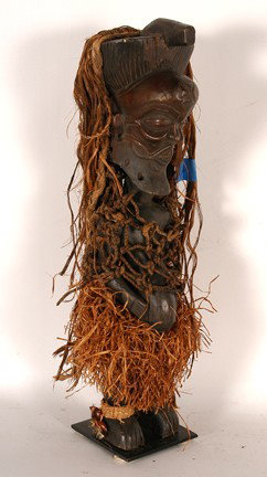 Tschokwe Tribe Fetish.: Carved wood, grass, rope. 18" x 4" x 4". Est. $100-200. Ship: $35. Standing male fetish figure with basketry ankle bracelets with cola nuts & feathers; raffia skirt (with complete genitals under skirt