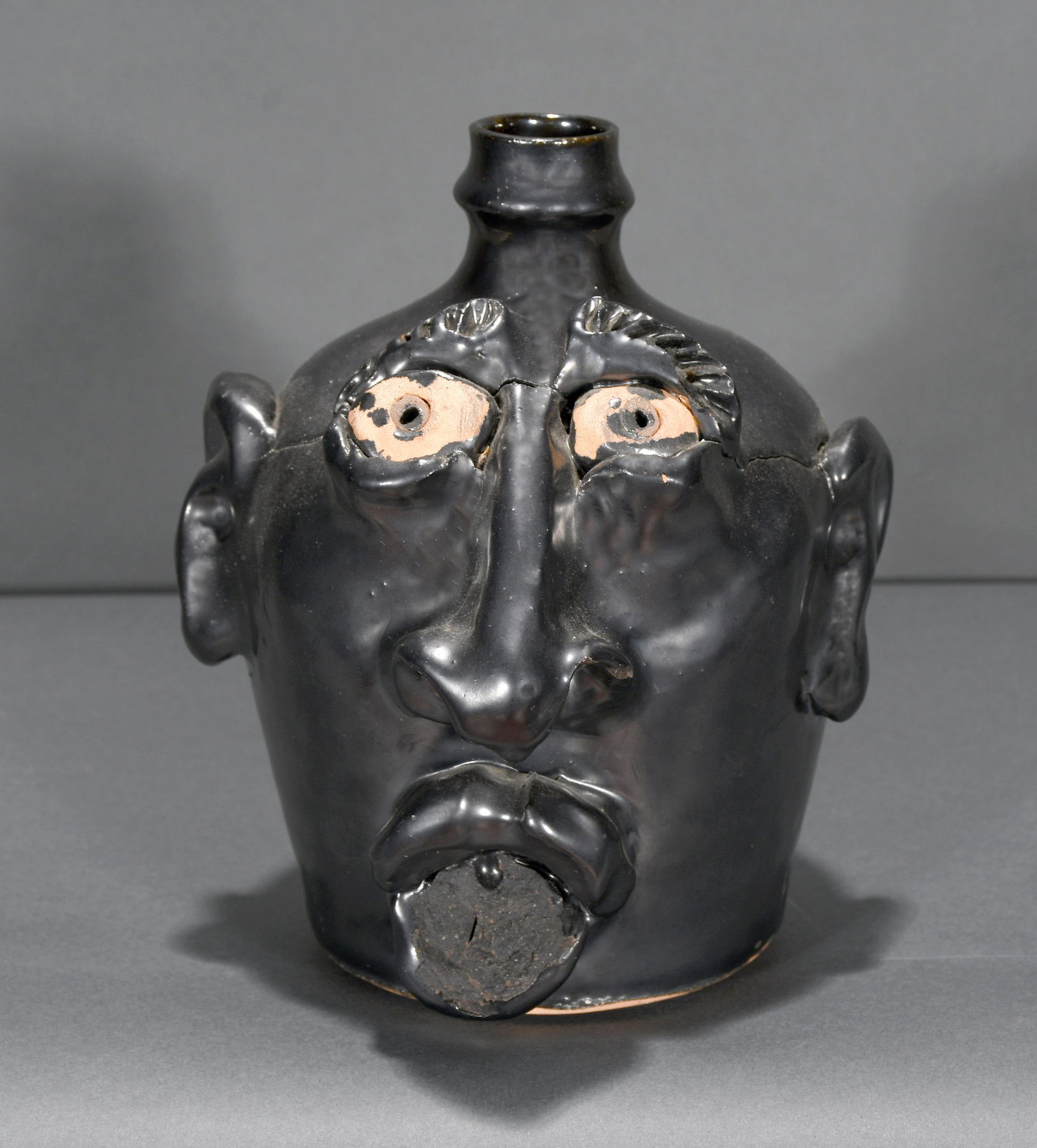 Billy Ray Hussey. Gun Metal Black Glaze Face Jug.: Billy Ray Hussey. Gun Metal Black Glaze Face Jug. Initialed and numbered, #6. Possible firing kiln loss at lower mouth and shrinkage near eyes and bridge of nose, otherwise good condition. 9" h. Est. 