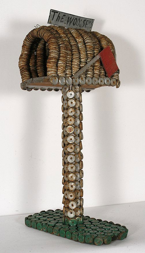 Clarence Woolsey. Woolsey’s Mailbox and Stand.: Clarence Woolsey. Woolsey’s Mailbox and Stand. Signed. Not dated. Bottlecap and wood construction with some paint. There is some loss of caps on back and red flag is not attached, otherwise good to
