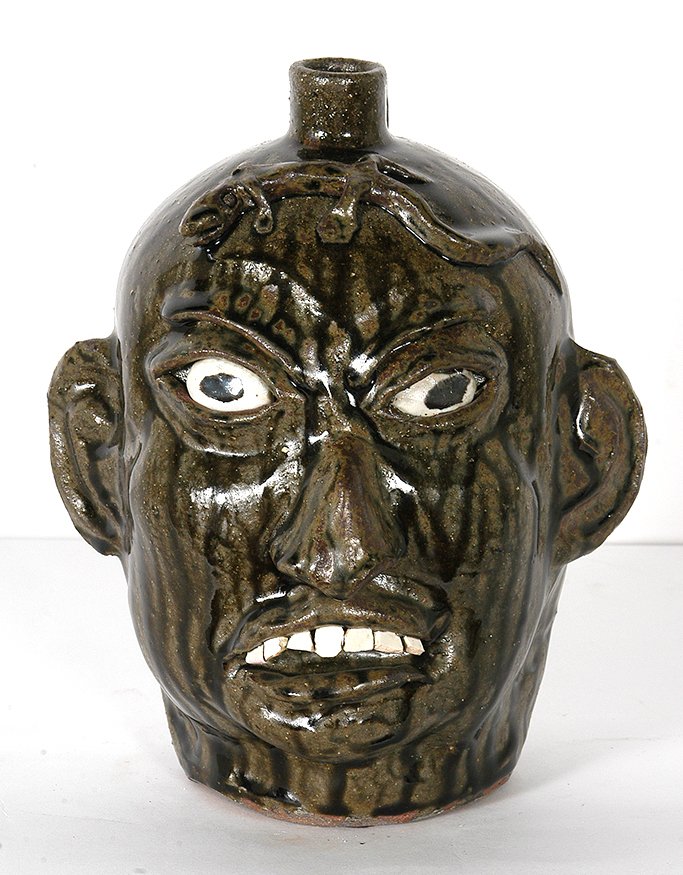 Chester Hewell. Lizard Face Jug.: Chester Hewell. Lizard Face Jug. 1993. Stamped and dated. Face with seven teeth and lizard on heard. Two tone green alkaline glaze with tobacco-spit drips. 11”h. Mint condition. Est. $200-300. Ship: