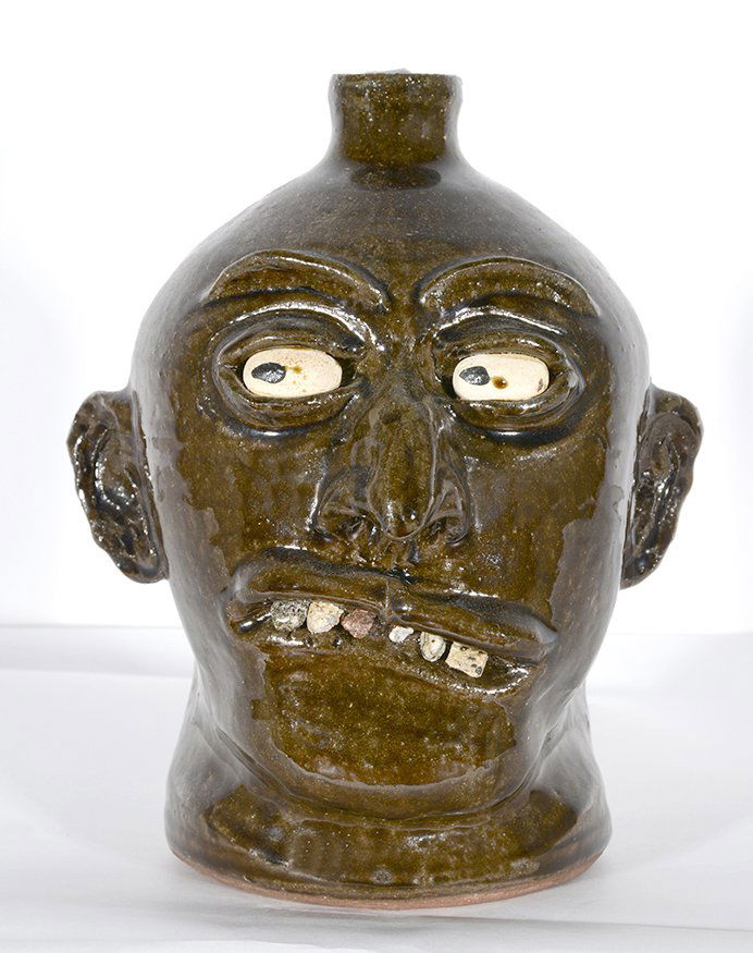 Lanier Meaders. Early Eyes Rock Tooth Face Jug.: Lanier Meaders. Early Eyes Rock Tooth Face Jug. c. 1960-70. Signed. Dark heavy glaze with crooked smile. One tooth lost in firing, otherwise excellent condition. 10”h. Est. $2,000-3,000. Ship: $55