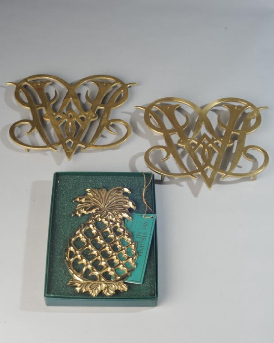 Three Virginia Metalcrafters Brass Trivets: Two are Colonial Williamsburg 10-10 Queen Ann Cypher copyright 1950, one is Colonial Williamsburg Pineapple copyright 1999 in presentation box. Largest: approx. 9" x 10 1/2".