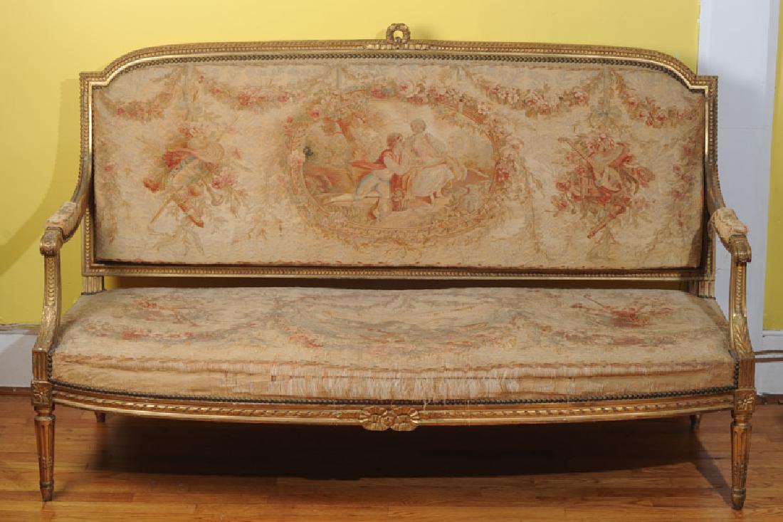 Louis XVI Style Settee: Carved giltwood, padded arms with scrolled handholds, Aubusson style tapestry upholstery shows wear commensurate with age. H: approx. 40". W: approx. 63". D: approx. 25".