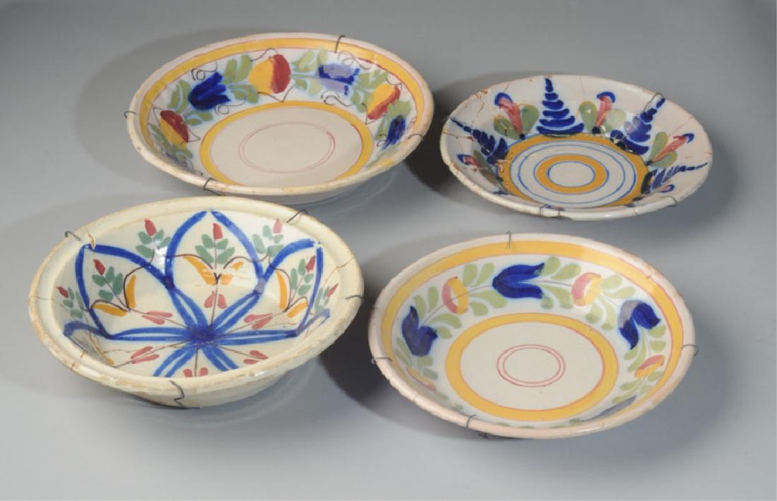 Lot of 19th C Spanish Pottery Bowls: Four antique Spanish tin-glazed bowls, probably from Manises. Decorated with a loose but sure hand in sunny yellows,greens, reds, and cobalt blue on creamy white ground. Two bowls have early iron stap