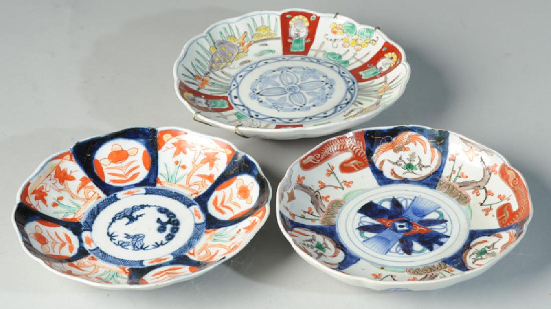 2 Antique Japanese Imari Scalloped Edge Plates: One with birds, bats, prunus and other motifs in underglaze blue, red, gold, green, brown, black and orange. The other with panels of flowers surrounding a central foliate design in underglaze blue wi