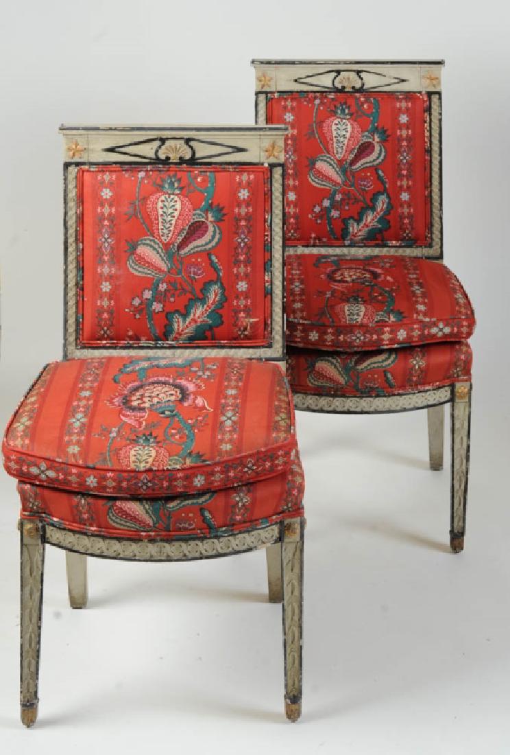 2 Classical Style Painted French Side Chairs: Wood painted white with blue and gold trim, square back, crest with central diamond panel, upholstered panel back and bowed seat, frame with guilloche band, tapered legs with foliate carving and roset