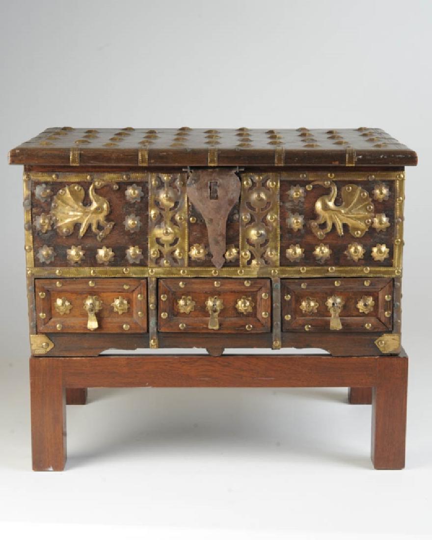 19th C. Asian Teakwood Chest: Teakwood chest with brass studs and bindings, hinged lid, carved top with conforming front with sunken panels and metal pulls, metal handles attached to ends, resting on 20th century stand. Chest H: a