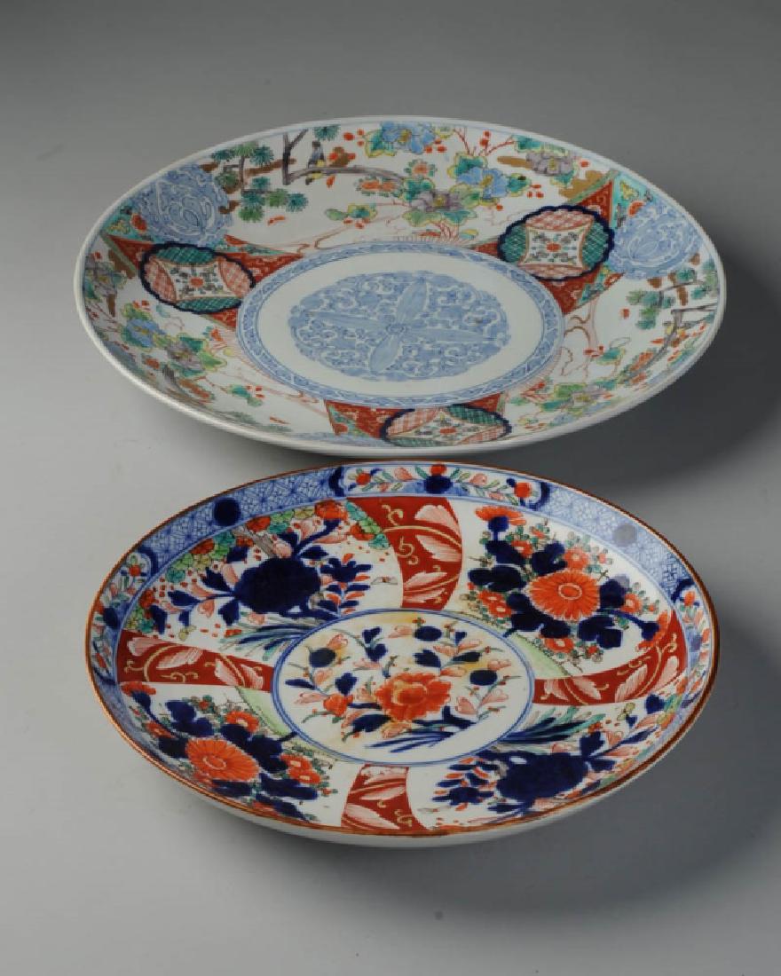 2 Antique Imari Chargers: Smaller with foliage and flowers in underglaze cobalt blue with red and green and gilt enamels. Brown dressing to rim. Unmarked. Probably 19th C. Some orange discoloration to surface. Approx. 13" in d