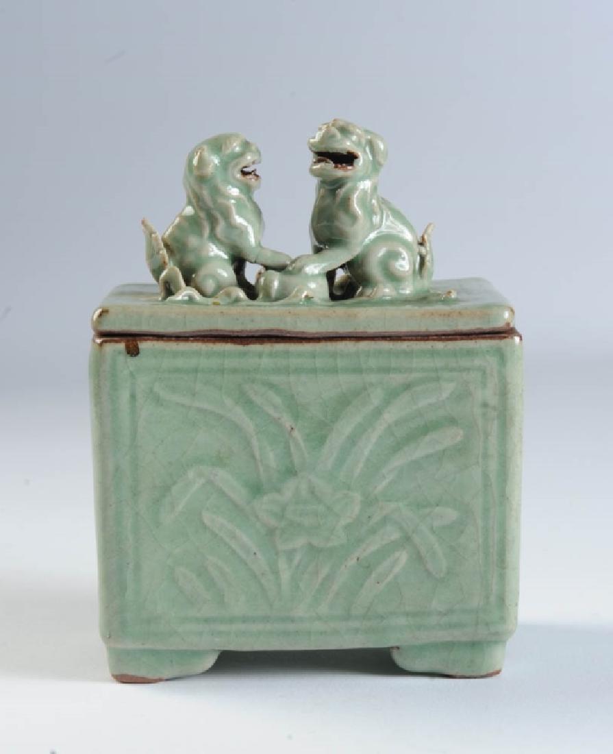 Chinese Longquan Celadon Square Censer: The sides carved or molded with lingzhi fungus and peony scrolls, the lid with a pair of finely modeled applied foo dogs, their paws on a brocade ball. Four low bracket feet. When the censer is covere