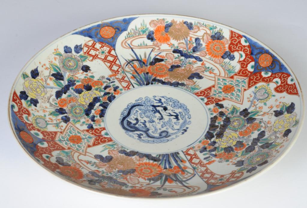 Large Antique Imari Charger: With central blue dragon amidst clouds and flames, surrounded by four reserves with chrysanthemums and peonies, underside of cavetto with feathers in blue. Excellent condition, with wear to gilt rim. 