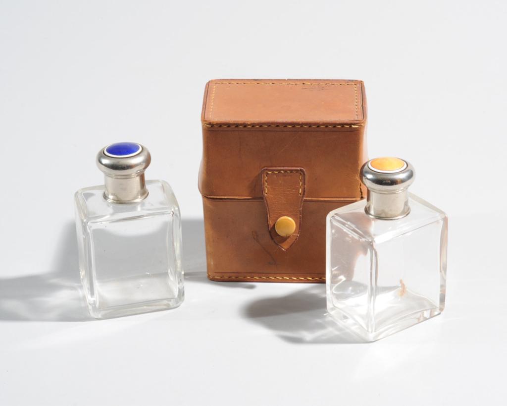 Pair Vintage Glass Perfume Bottles: With enamel-decorated caps and leather case, minor chips to stoppers, damage to leather case, in as found condition. Case: approx. 4" x 3 1/2" x 2 1/2".