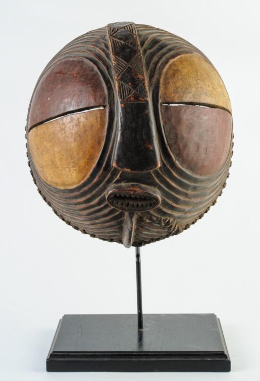 Luba Round Kifwebe Mask: Carved wood and pigments. On gallery stand. Approx. 14" diameter. Provenance: Estate of Thomas McNemar, (1931-2019.) McNemar lived and collected throughout Central and West Africa in the 1960s and 70s