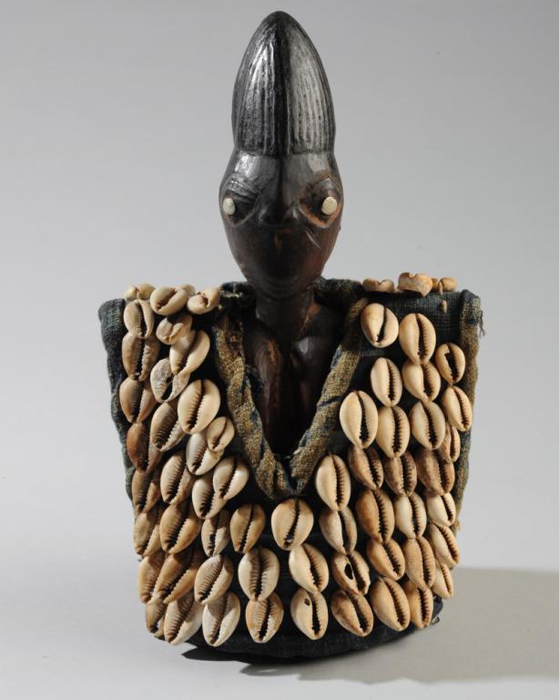 Yoruba Ibeji Twin Figure: Female figure, carved wood with metal eyes, wearing a garment of fabric covered with cowrie shells, beneath her clothes beads and shells strung around her ankle and waist. Approx. 10 1/2" in height. P