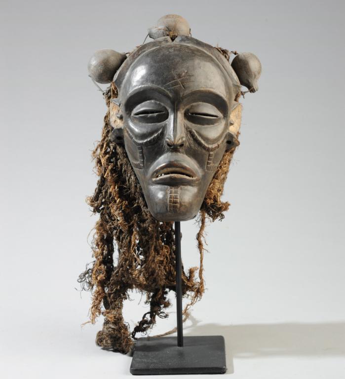 Chokwe Mwana Pwo Mask: Carved wood with fiber rope netting and small gourds. On gallery stand. Mask, approx. 8" x 6". Provenance: Estate of Thomas McNemar, (1931-2019.) McNemar lived and collected throughout Central and Wes