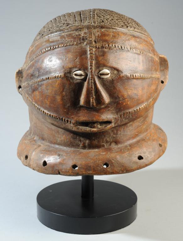 Tabwa Helmet Mask: Large anthropomorphic helmet mask with cowrie shell eyes, flattened nose, open mouth with tongue visible, radial facial scarification, carefully carved hair. Tabwa people, Democratic Republic of Congo