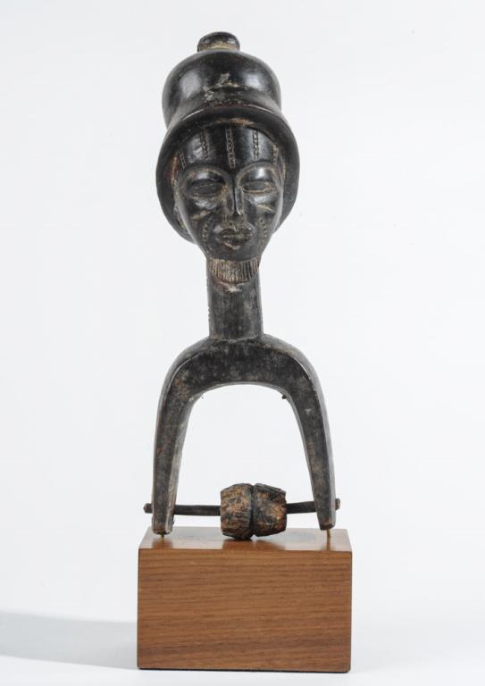 Baule African Heddle Pulley: Figural heddle pulley showing a Baule male wearing a helmet. The face shows idealized, refined features with facial and neck scarification and neat beard. In place of the usual carefully coiffed hair 