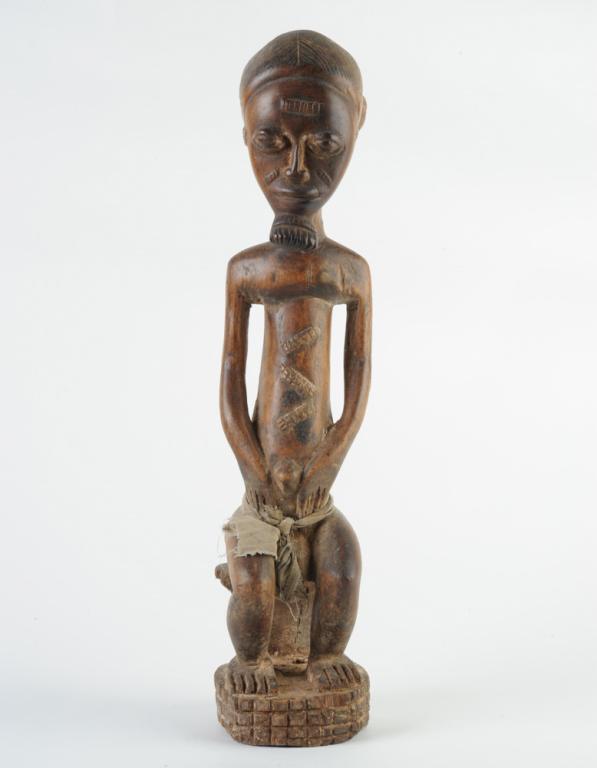 Baule Male Statue: Carved wood figure of a seated man, with gentle expression, beard, facial and body scarification, long torso. Fabric garment tied around his waist. Ivory Coast. Approx. 18 1/2" in height. Provenance: 