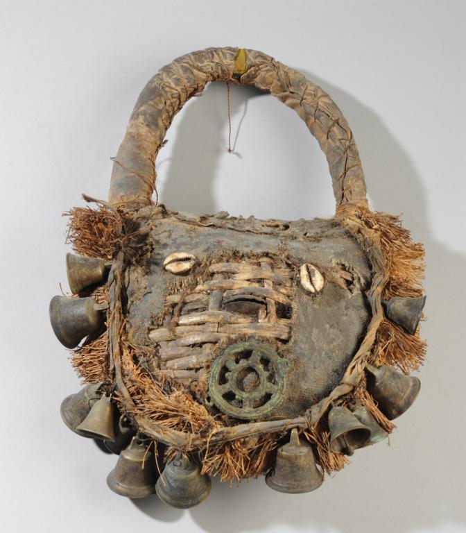 Senufo Hand Mask: Hand mask with woven cane frame covered with fabric and animal hide, with cowrie 'eyes' and metal objects seeming to represent nose and mouth, with a fringe of raffia and strung with metal bells, and