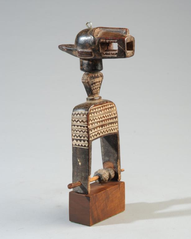 Baule African Heddle Pulley: Beautifully carved pulley in the form of a Bo Nun Anuin mask topping placed atop a body with relief carved geometric decorations. Baule people, Ivory Coast. On gallery stand. Pulley, approx. 8" H. Pro
