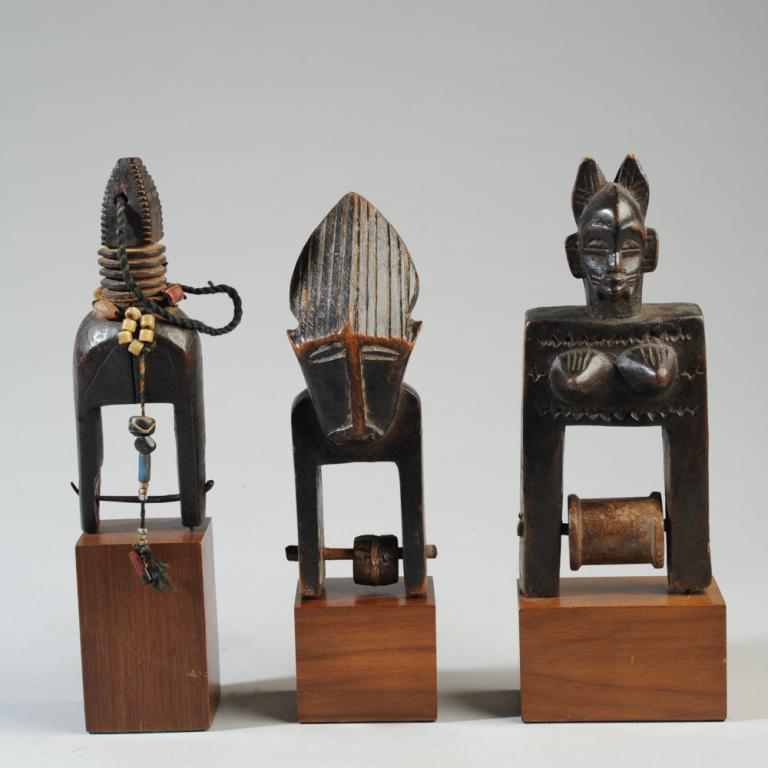 Three West African Heddle Pulleys: Two with mask heads, the third of geometric form, embellished with a string of beads. All on gallery stands. Pulleys, approx. 6 3/4" to 7 3/4" in height. Provenance: Estate of Thomas McNemar, (1931-20