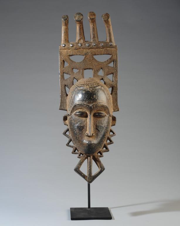African Fine Yaure Mask, Ivory Coast: Delicate facial features with arched brows, coffee bean eyes, long slender nose, pouting mouth, with high comb headdress above carefully coiffed hair, embellished with tacks and pieces of tin. Excelle