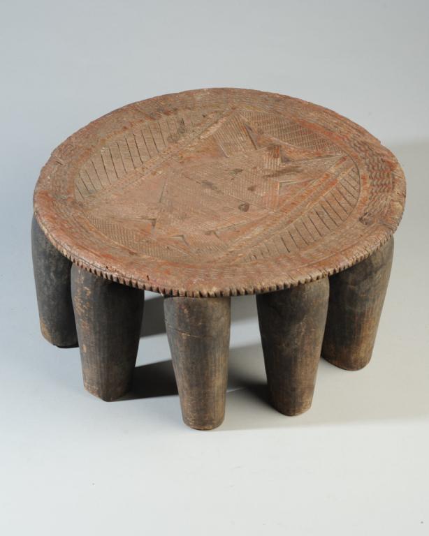 African Nupe Stool, Nigeria: Round slightly concave stool with ten slightly tapering legs, the top with intricate relief carved and incised geometric decoration. Well worn. Approx. 14" diameter, 6 3/4" in height. Provenance: Esta