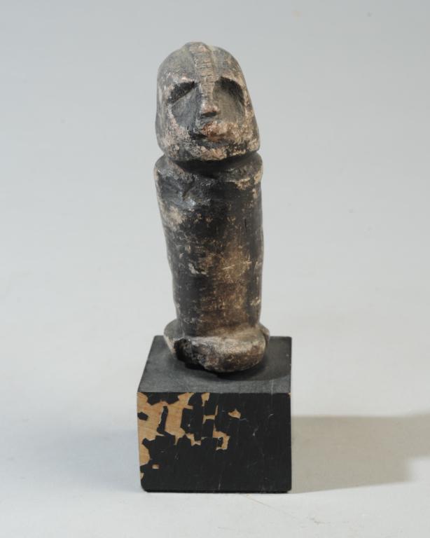 Kissi Stone Figure Pomdo / Nomoli: Small carved soapstone figure of somewhat phallic form, with helmet-shaped head with notched cranial ridge from nose to nape of neck, and with cylindrical body. Black pigment applied to stone. Kissi s