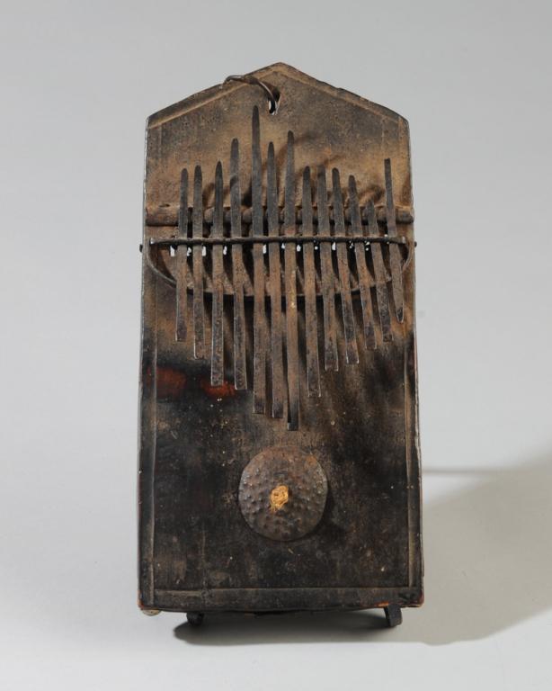 African Kalimba Thumb Piano: Fang kalimba, dark lustrous patina. On gallery stand. Approx. 10 1/2" x 5 1/4" x 1". Provenance: Estate of Thomas McNemar, (1931-2019.) McNemar lived and collected throughout Central and West Africa i