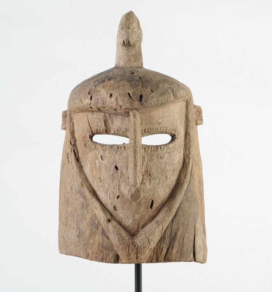 African Dogon Helmet Mask: The shield-shaped face with narrow slit eyes rimmed with small raised triangles, suggestive of eyelashes, and with long, arrow shaped nose, no mouth, tiny high placed ears, the whole face as if in a c